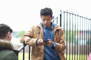 Young Male College Student Reading Smartphone Text On Campus