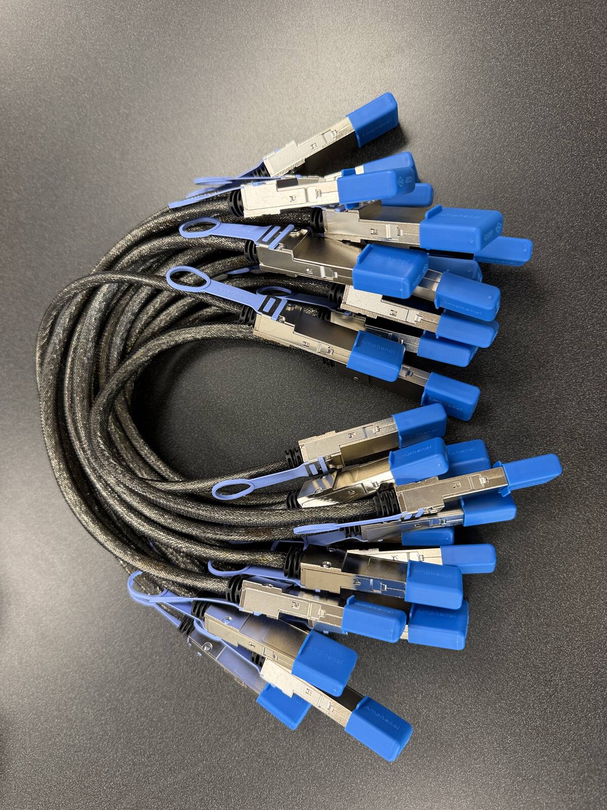 Stack of genuine Amphenol QSFP112 400G DAC cluster cables with blue pull tabs in Petronella Technology Group stock